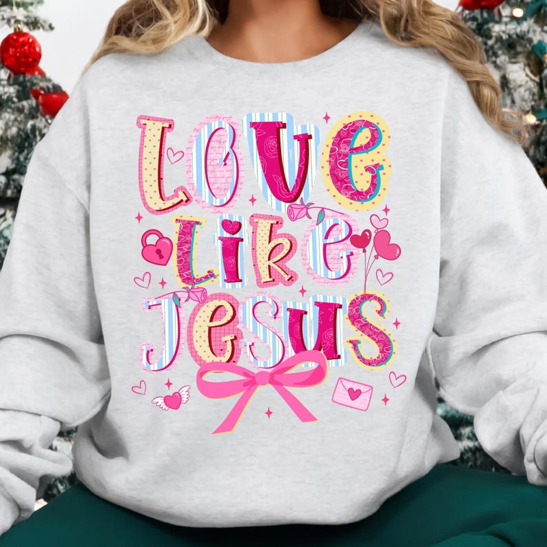 May include: A light gray sweatshirt with the words "LOVE LIKE JESUS" in a colorful, whimsical font. The design includes hearts, a lock, a bow, and an envelope. The letters are in pink, yellow, blue, and white.