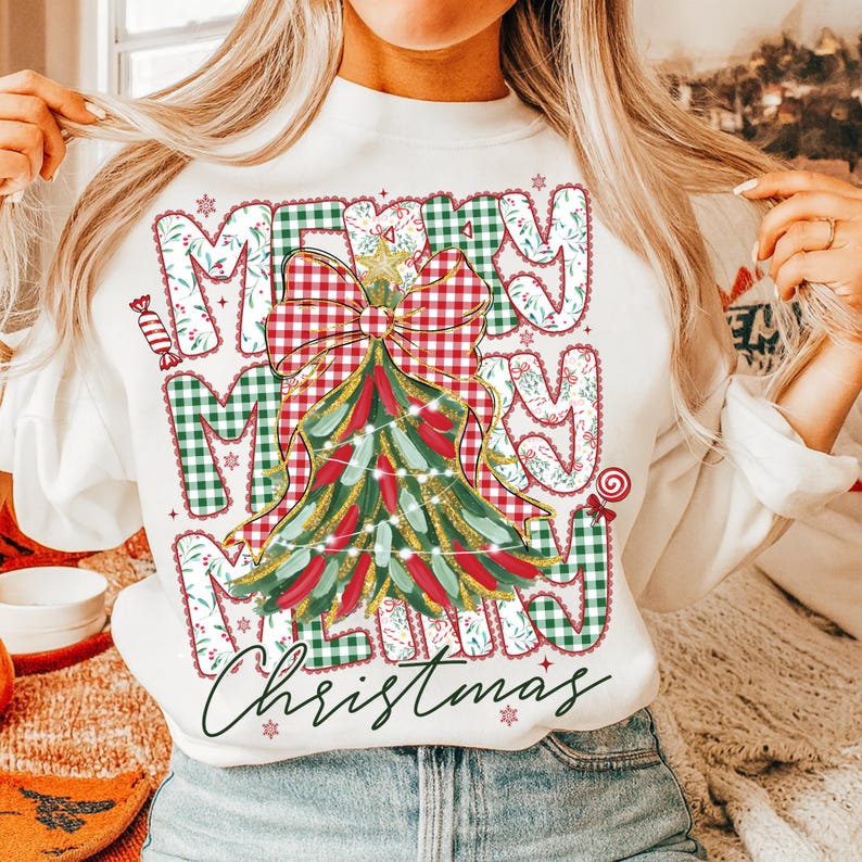 May include: White sweatshirt with a festive Christmas design. The design features the words "Merry Christmas" in a mix of plaid and floral patterns, with a Christmas tree and bow in the center. The sweatshirt is a comfortable, casual style.