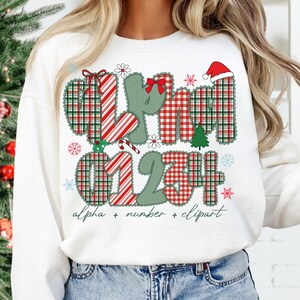 May include: White sweatshirt with a Christmas-themed design. The design features the letters "XHM" and numbers "01234" in a plaid pattern, along with snowflakes, a Santa hat, and a Christmas tree. The text "alpha + number + clipart" is also included.