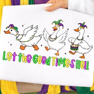 May include: White fabric featuring three cartoon geese in Mardi Gras attire. The geese wear jester hats and beaded necklaces. One goose plays a drum. The text "Let the Good Times Roll" is below the geese.