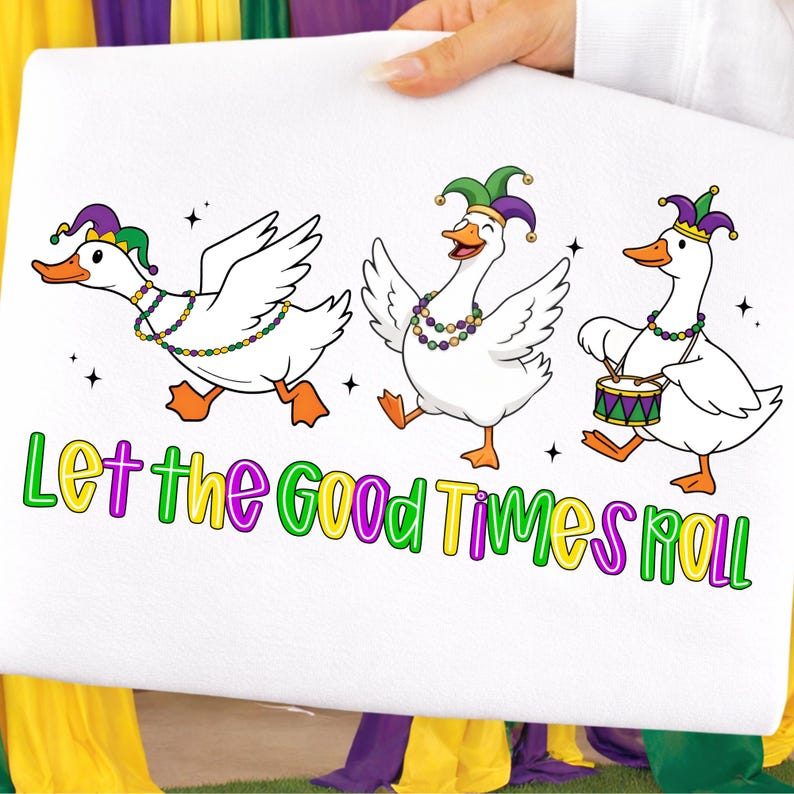 May include: White fabric featuring three cartoon geese in Mardi Gras attire. The geese wear jester hats and beaded necklaces. One goose plays a drum. The text "Let the Good Times Roll" is below the geese.