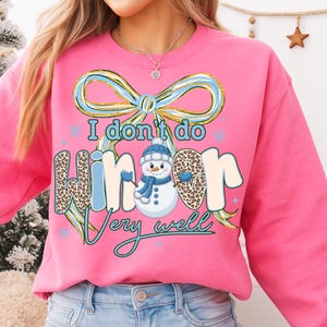 May include: Pink sweatshirt with the text "I don't do winter very well" and a snowman graphic. The word "winter" has a leopard print pattern. The design includes a blue bow and snowflakes.