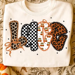May include: Cream-coloured sweatshirt with the word "LOVE" in a decorative design. The letters feature leopard print, a black and white checkerboard pattern, and cherry illustrations. The letters are outlined with black lace and adorned with orange bows.