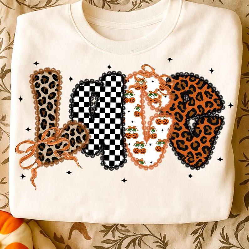 May include: Cream-coloured sweatshirt with the word "LOVE" in a decorative design. The letters feature leopard print, a black and white checkerboard pattern, and cherry illustrations. The letters are outlined with black lace and adorned with orange bows.