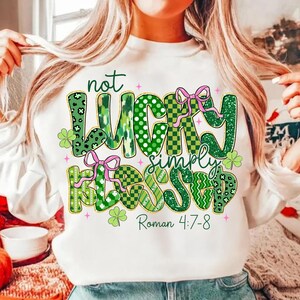 May include: White sweatshirt with the text "not LUCKY simply BLESSED" in green, with pink bows and shamrock accents. The text "Roman 4:7-8" is also printed on the shirt. The sweatshirt is a St. Patrick's Day theme.