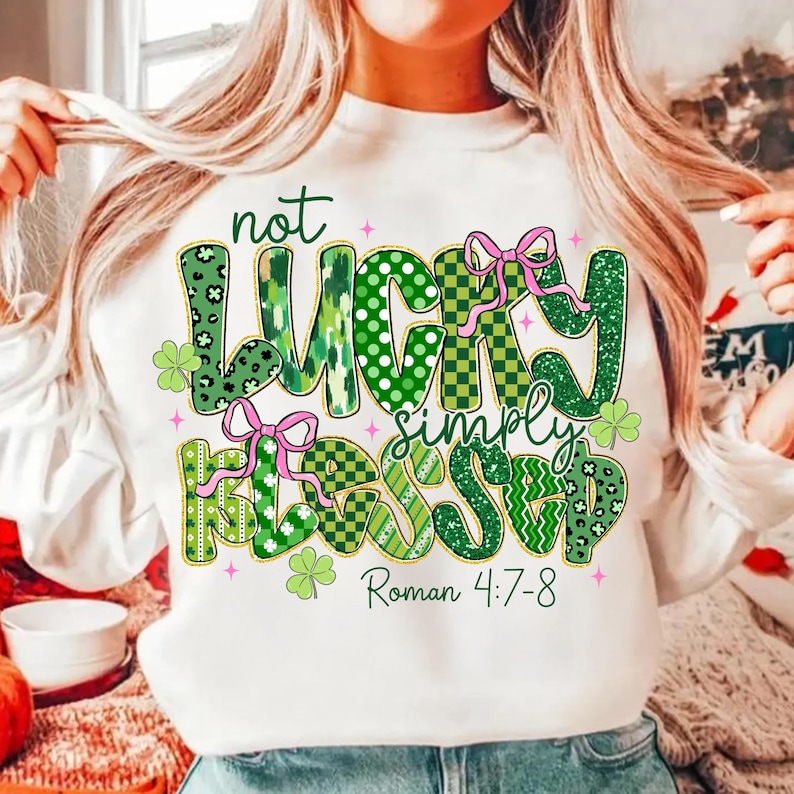 May include: White sweatshirt with the text "not LUCKY simply BLESSED" in green, with pink bows and shamrock accents. The text "Roman 4:7-8" is also printed on the shirt. The sweatshirt is a St. Patrick's Day theme.