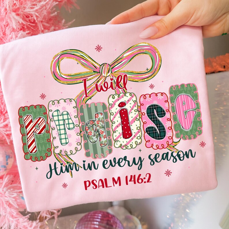 May include: A light pink t-shirt with the words "I will Praise Him in every season" in a decorative font. The design includes a bow and snowflakes. Psalm 146:2 is printed below the text.
