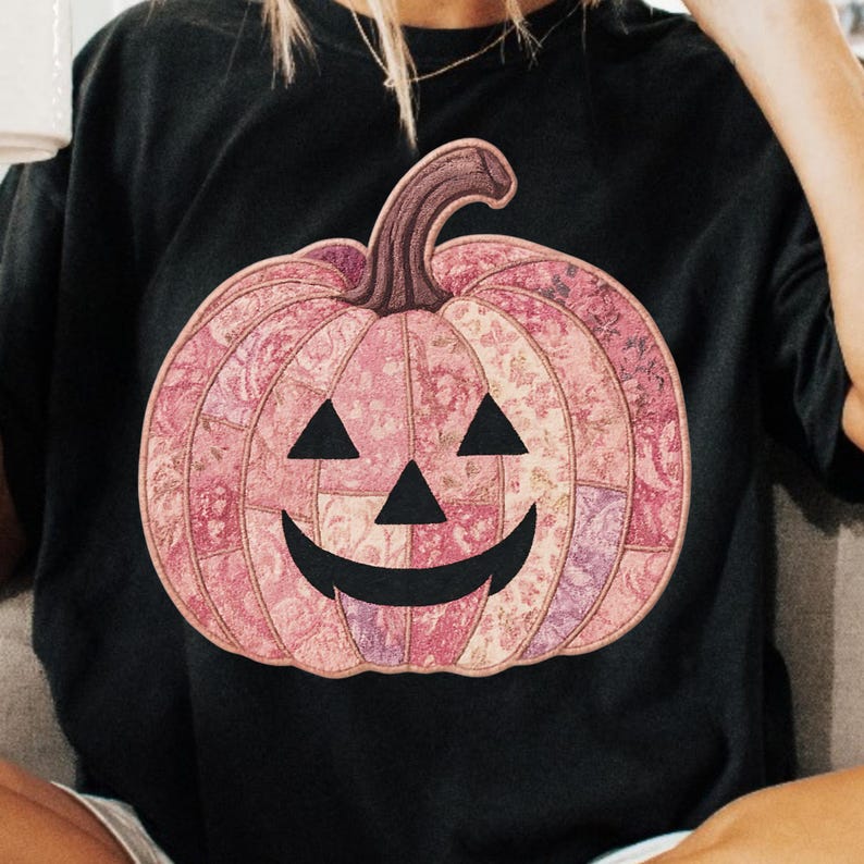 K&ouml;nnte beinhalten: Schwarzes T-Shirt mit einem rosa K&uuml;rbis-Design. Der K&uuml;rbis hat ein Patchwork-Muster in Rosa- und Lilat&ouml;nen mit einem geschnitzten Gesicht. Der Stiel ist braun. Eine Halloween-Grafik.
