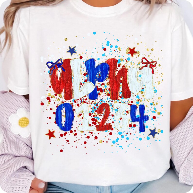 May include: White t-shirt with the word "Alpha" in red, white, and blue, and the numbers "01234". The design includes red, blue, and gold accents, with star and bow details. The shirt is a casual style.