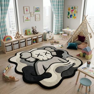 May include: A large, irregularly shaped area rug featuring a stylised character with a skull-like head and X-shaped eyes. The design uses a palette of black, dark grey, light grey, and cream, with a thick black border defining the organic shape.