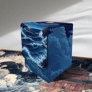 Op de afbeelding: Een rechthoekige opbergdoos met een donkerblauwe oceaan-scène met beukende witte golven en een verre maan op het deksel. De zijkanten tonen een diepblauw wolkenpatroon en de doos staat op een mat met een afbeelding van een traditionele tempel.