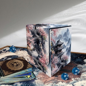 Könnte beinhalten: Eine quadratische Aufbewahrungsbox mit einem japanisch inspirierten Landschaftsdesign mit einer Pagode, Bergen und Kirschblüten. Die Box ist von blauen Würfeln und einem Kartenspiel mit einem Drachendesign umgeben.