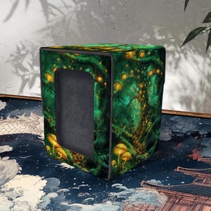 Könnte beinhalten: Ein würfelförmiger Aufbewahrungskasten mit einem Fantasy-Design. Die Box hat einen dunkelgrünen Hintergrund mit leuchtenden gelben Pilzen und Bäumen. Der Innenraum ist schwarz, und die Box steht vor einem strukturierten Hintergrund.