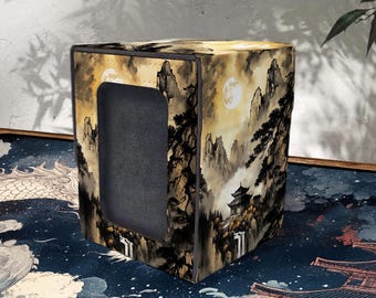 May include: A square storage box with a landscape design featuring mountains, trees, and a full moon. The box has a dark gray interior and a rectangular opening on one side. The color palette includes shades of brown, beige, and black.