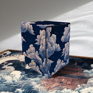 Puede incluir: Una caja azul oscuro con un patrón de nubes y estrellas celestiales. La caja tiene forma de cubo con una tapa con bisagras. El fondo presenta un dragón y un edificio de estilo japonés.