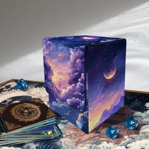 May include: A cube-shaped card storage box with a celestial design featuring a night sky, clouds, and a crescent moon. The box is surrounded by playing cards, dice, and a playmat with a dragon design.