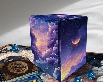 Puede incluir: Una caja de almacenamiento de cartas en forma de cubo con un diseño celestial que presenta un cielo nocturno, nubes y una luna creciente. La caja está rodeada de cartas, dados y una alfombrilla de juego con un diseño de dragón.