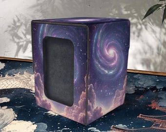 May include: A cube-shaped storage box with a celestial design. The box features a dark purple background with a swirling galaxy pattern and white stars. The bottom of the box has a cloud design. The box has a rectangular opening.