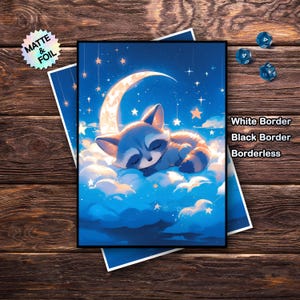May include: A print featuring a sleeping raccoon on a cloud under a crescent moon and stars. The artwork has a blue and white color scheme. Text on the print reads "White Border, Black Border, Borderless". A holographic sticker that says "Matte & Foil" is also present.