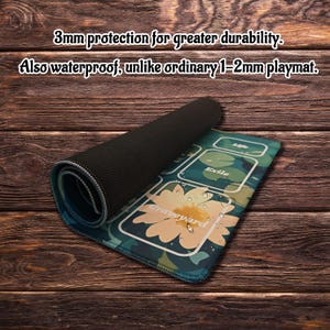 May include: A rolled-up playmat with a floral design and the word "Graveyard". The mat is teal, white, and yellow, with the text "3mm protection for greater durability. Also waterproof, unlike ordinary 1-2mm playmat."