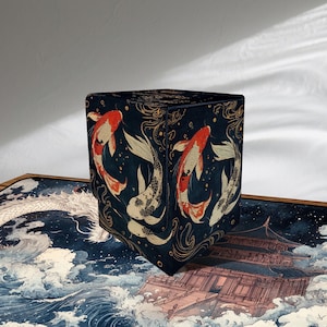 May include: A dark blue cube-shaped storage box with a Japanese koi fish design. The box features red, white, and gold koi fish illustrations on a dark blue background. The box is likely made of fabric or a similar material.