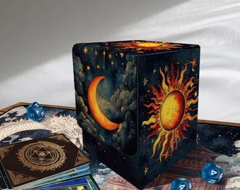 Puede incluir: Una caja de almacenamiento de cartas azul oscuro, con textura de terciopelo, con un diseño celestial que presenta una luna creciente, un sol, estrellas y nubes. Dados azules y una baraja de cartas la rodean.