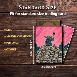 Puede incluir: Fundas rosas para cartas coleccionables con una ilustraci&oacute;n de un personaje verde sosteniendo un bast&oacute;n, sobre una pila de calaveras. Las fundas miden 91 mm por 66 mm. El texto dice "STANDARD SIZE" y "Fit for standard size trading cards."