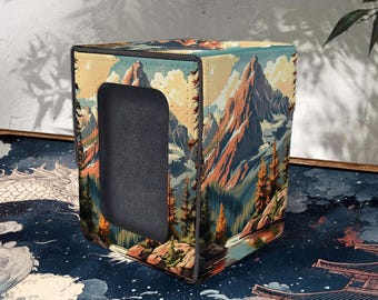 May include: A square storage box with a mountain landscape design. The box features a large rectangular opening and is decorated with a colorful illustration of mountains, trees, and a river. The box is stitched with brown thread.