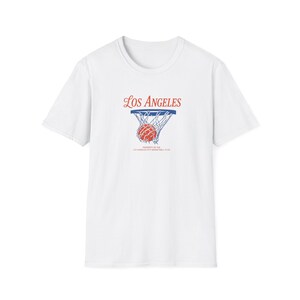 May include: A white short-sleeve t-shirt featuring a graphic of a basketball going through a hoop. The text reads Los Angeles in red script above the hoop, and Property of the Los Angeles City Basketball Club in small black text below the hoop.