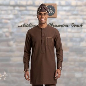 May include: A brown long-sleeved tunic with a mandarin collar and a single chest pocket, paired with matching brown trousers and a brown patterned cap. The outfit features clean lines and a solid colour palette, creating a coordinated ensemble.