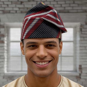 May include: A patterned, triangular-shaped hat with red, black, white, and yellow stripes. The hat is worn on the head and has a folded-over brim. The hat is made of a woven fabric and is likely a traditional or cultural garment.