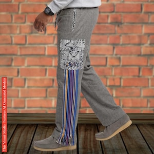 May include: Grey trousers featuring a rectangular patch on the thigh with a black and white geometric pattern, accented by a long, vertical multi-colored striped fabric panel with fringe detailing at the bottom hem and a drawstring waist.