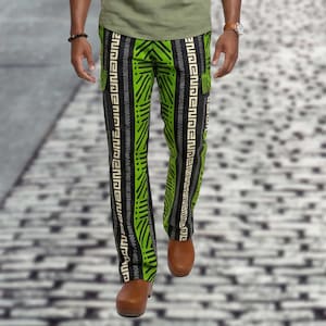 May include: Green and black patterned pants with vertical stripes and the word "INDEPENDENCE" printed in white. The pants are worn with brown clogs. The pants have a bold, geometric design.