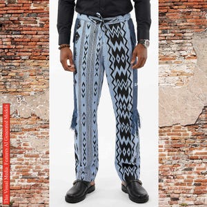 May include: Light blue trousers featuring a prominent black and white geometric pattern with vertical stripes and zig-zag motifs. The pants include a drawstring waist, side pockets, and decorative fringe accents hanging from the mid-thigh area.