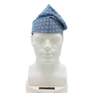May include: A blue and white patterned hat with a unique, folded design. The hat is displayed on a white mannequin head, showcasing its shape and texture. The fabric appears to be a woven material, offering a textured appearance.