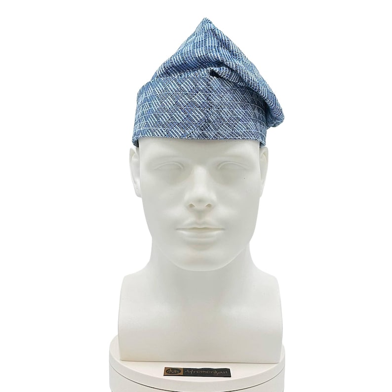 May include: A blue and white patterned hat with a unique, folded design. The hat is displayed on a white mannequin head, showcasing its shape and texture. The fabric appears to be a woven material, offering a textured appearance.