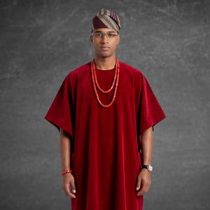 May include: A person wearing a red velvet tunic with a matching red beaded necklace and bracelet. The person is also wearing a striped head covering and glasses. A watch is visible on the wrist.
