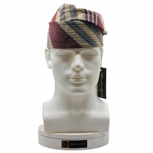 May include: A striped head wrap in burgundy, tan, and black, displayed on a white mannequin head. The fabric features a repeating pattern of vertical stripes. A black tag with white text hangs from the head wrap.