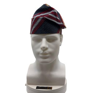 May include: A patterned hat with red, white, and navy blue stripes, displayed on a white mannequin head. The hat has a folded brim and a pointed crown. The fabric appears to be woven.