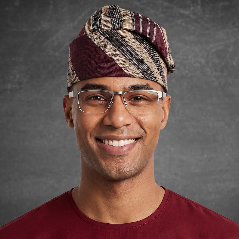 May include: A person wearing a burgundy and tan striped head wrap and silver-framed glasses. The person is smiling and wearing a burgundy shirt. The background is a solid gray.
