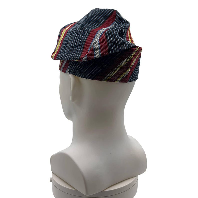 May include: A folded hat with a striped pattern in navy, red, and gold. The hat is displayed on a white mannequin head, highlighting the fabric's texture and design. The stripes on the hat run vertically, creating a striking visual effect.