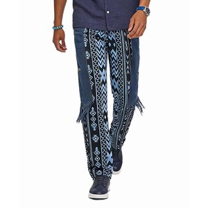 May include: Denim pants with a unique design featuring a mix of blue and black geometric patterns. The pants have fringe detailing along the sides and are paired with blue shoes. The overall style is casual and eye-catching.