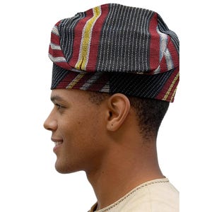 May include: A patterned hat featuring a black base with stripes of red, yellow, and white. The hat is worn by a person in profile, highlighting the hat's design and texture. The hat appears to be made of woven fabric.