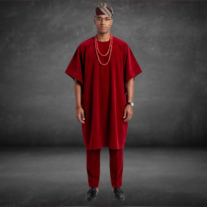 May include: A red velvet traditional outfit, including a tunic and trousers. The ensemble is complemented by a matching head wrap, beaded necklace, and bracelet. The outfit is paired with black shoes and a wristwatch.