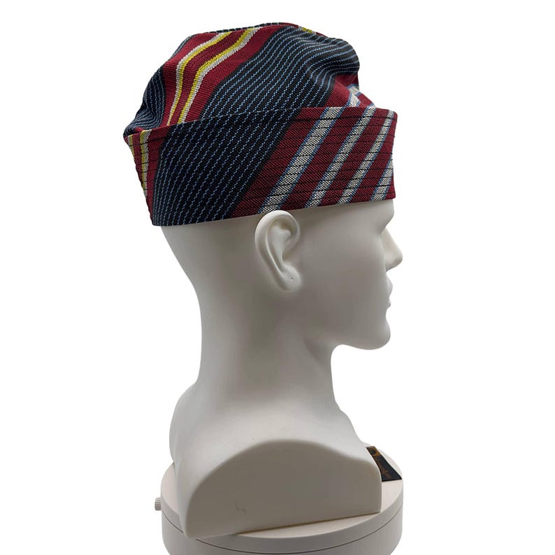 May include: A patterned hat with a rectangular brim. The hat features stripes of red, navy blue, yellow, and white. The hat is displayed on a white mannequin head.