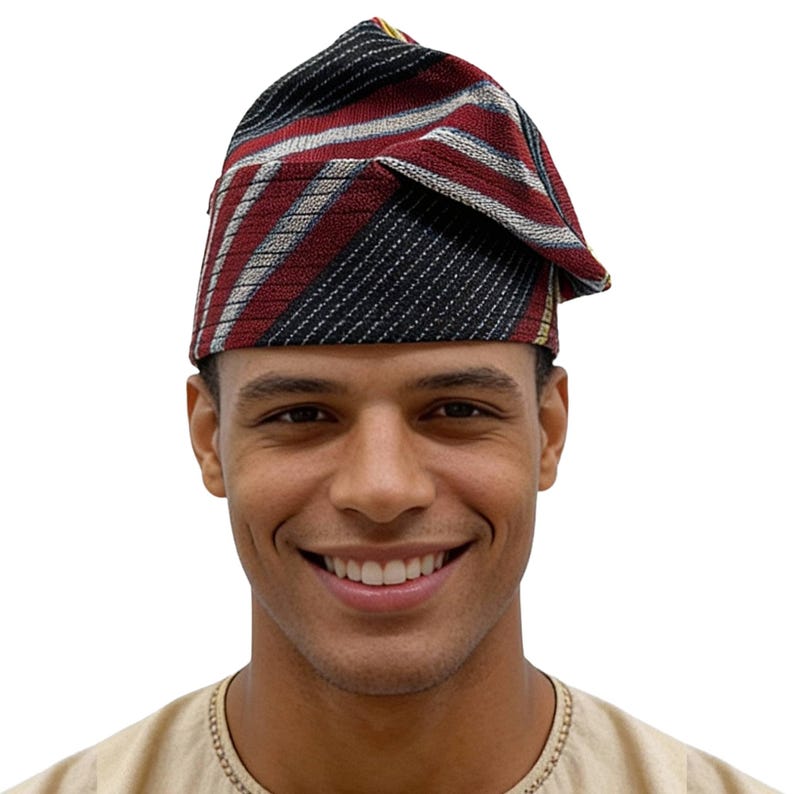 May include: A traditional African hat with a folded, triangular shape. The hat features a striped pattern in red, black, white, and gold. The fabric appears to be woven, with a textured surface.