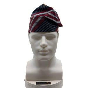 May include: A patterned hat with a folded brim, displayed on a white mannequin head. The hat features a design of diagonal stripes in navy blue, red, and white. The hat is a traditional style, likely for cultural or formal occasions.