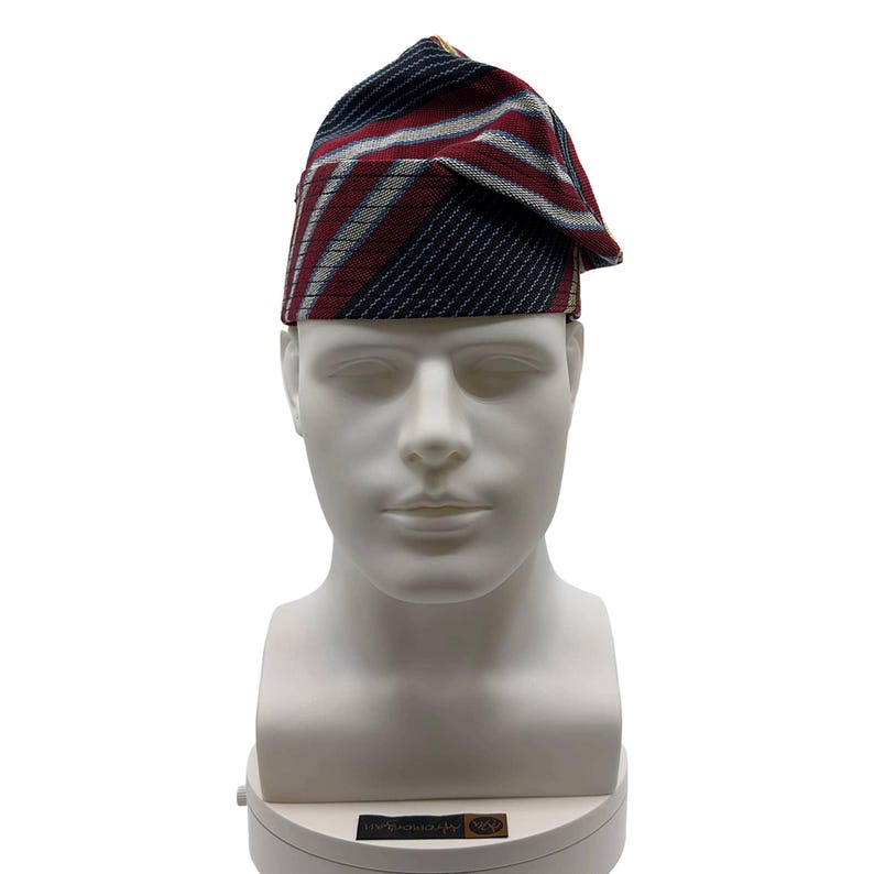 May include: A patterned hat with a folded brim, displayed on a white mannequin head. The hat features a design of diagonal stripes in navy blue, red, and white. The hat is a traditional style, likely for cultural or formal occasions.