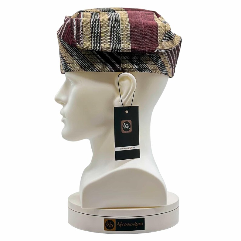 May include: A patterned hat with burgundy, tan, and black stripes is displayed on a white mannequin head. The hat has a rectangular shape with a folded brim. A black tag with a logo hangs from the hat.