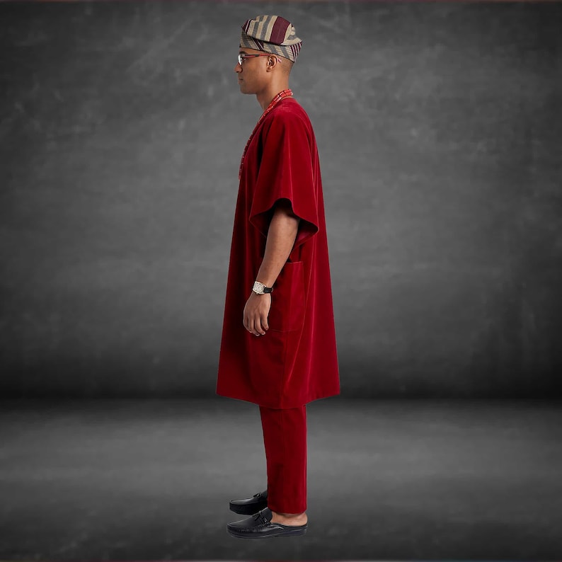 May include: A red velvet traditional outfit, including a tunic and pants. The outfit is paired with a striped head wrap and black shoes. A watch is visible on the wrist. The ensemble is a formal attire.